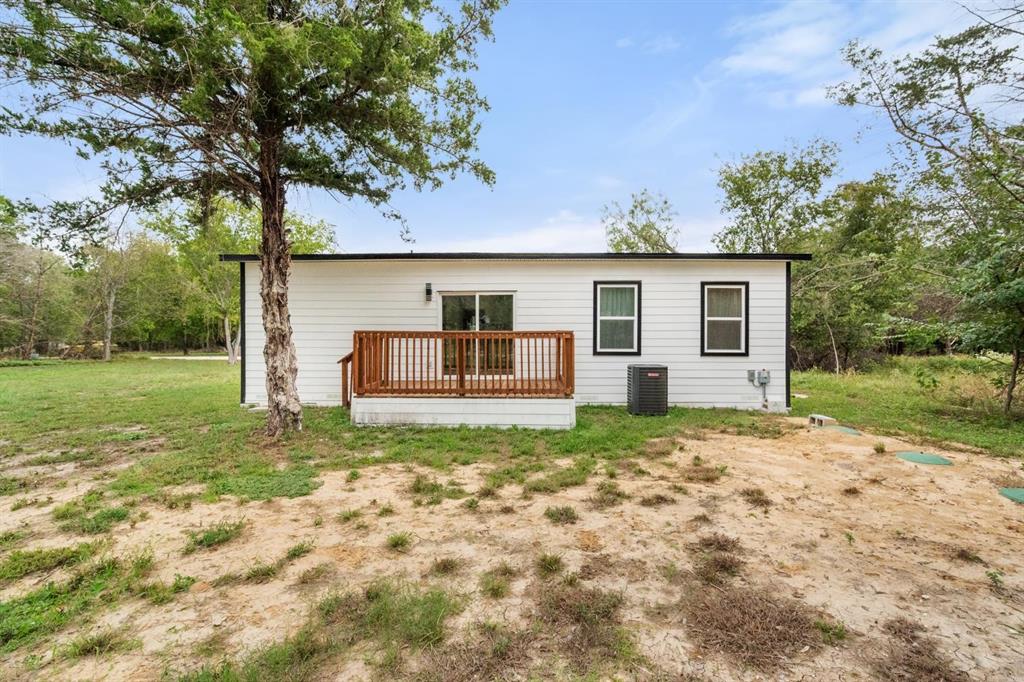 Exterior featuring white horizontal siding, dark window trim, a raised wooden deck with railings, and mature trees