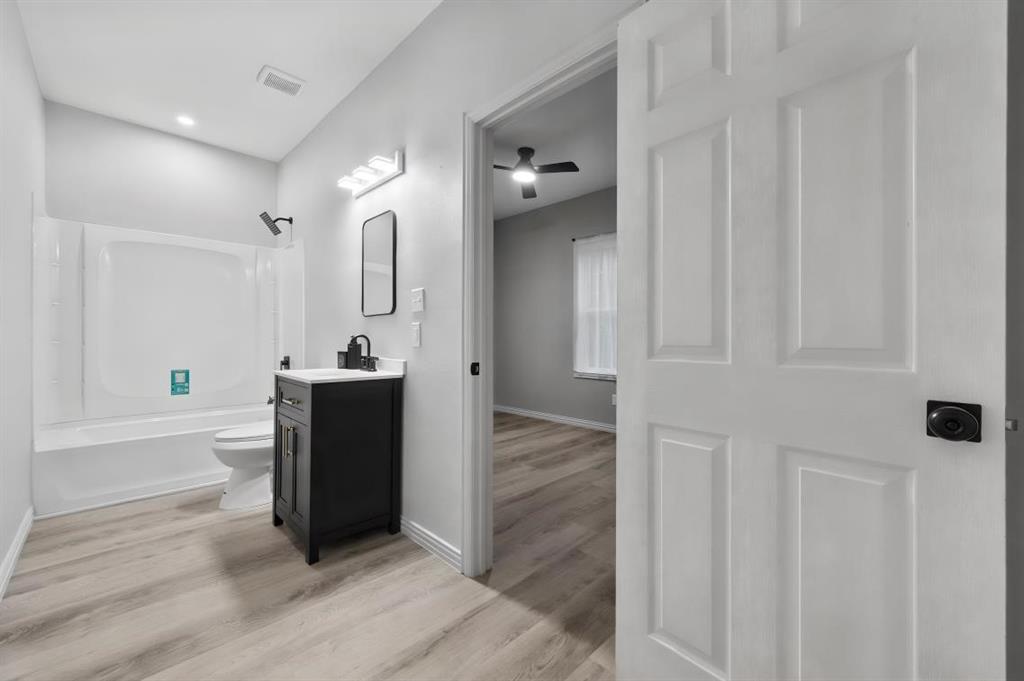 Bathroom featuring a black vanity with a contrasting white countertop, a black wall-mounted faucet, a white acrylic tub-shower combination, and wood-finish flooring