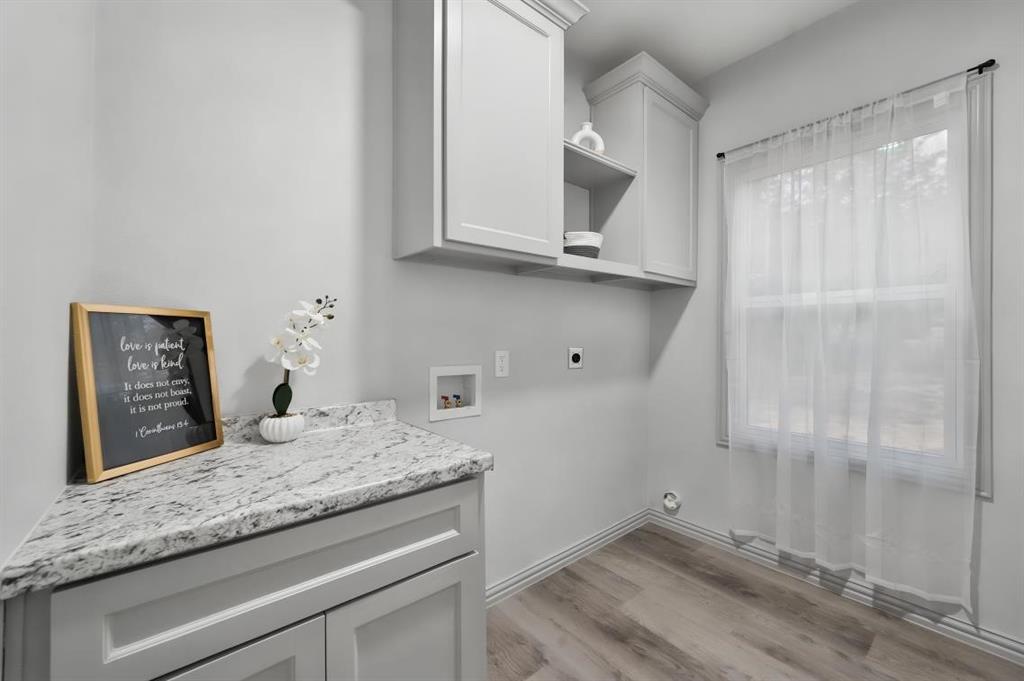 Utility area featuring light-toned cabinetry, a stone-finish countertop, upper wall-mounted storage cabinets, and wood-finish flooring