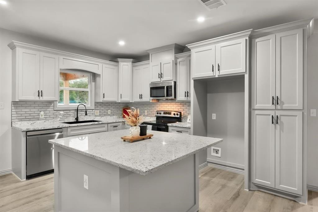 Kitchen featuring shaker-style cabinetry, a central island with a stone-finish countertop, stainless steel appliances, a light-toned brick-pattern backsplash, and wood-finish flooring