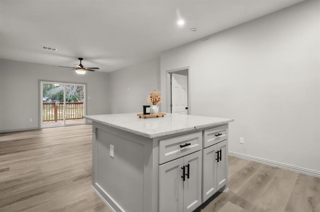 Kitchen island featuring light-toned cabinetry, light-flecked stone countertop, and matte black hardware, paired with wood-finish flooring and sliding glass doors