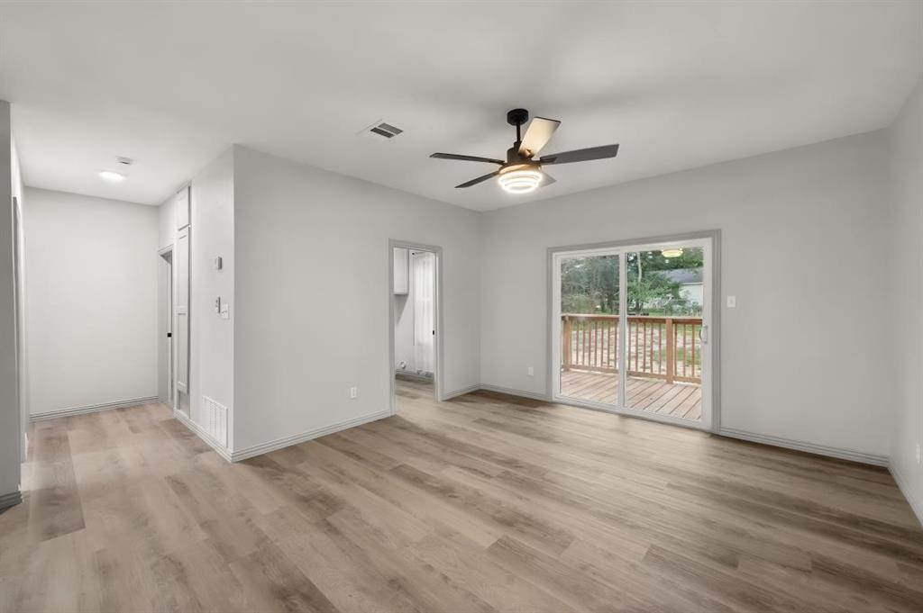 Neutral interior featuring wood-finish flooring, a contemporary ceiling fan with integrated lighting, and sliding glass doors leading to an exterior wood deck