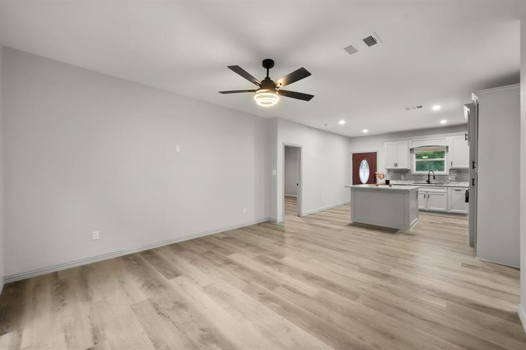 Open-concept interior featuring wood-finish flooring, a central kitchen island, recessed lighting, and a modern ceiling fan