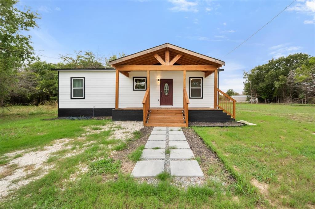Exterior featuring horizontal white siding, a contrasting dark base, a wood-frame covered porch with gable detailing, a decorative glass-insert entry door, and a stone paver walkway