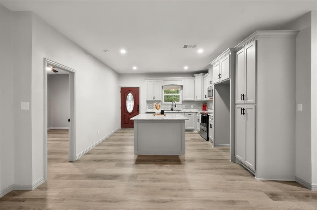 Kitchen featuring white cabinetry, center island with stone-finish countertop, light-toned wood-finish flooring, recessed lighting, and stainless steel appliances