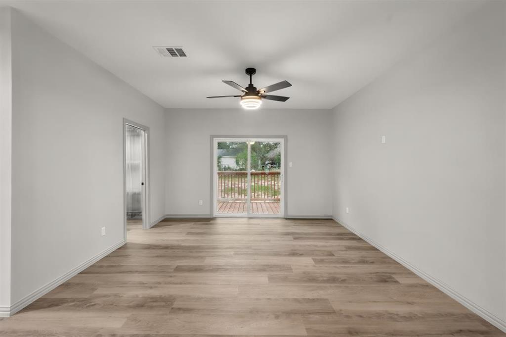 Neutral-toned interior featuring wood-finish flooring, a ceiling fan with integrated lighting, and a sliding glass door providing access to a deck