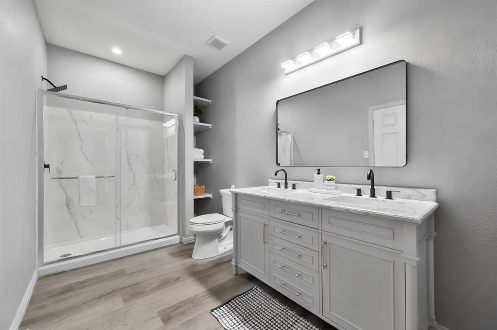 Bathroom featuring a dual-sink vanity with stone countertop, matte black fixtures, walk-in shower with glass enclosure, and built-in shelving