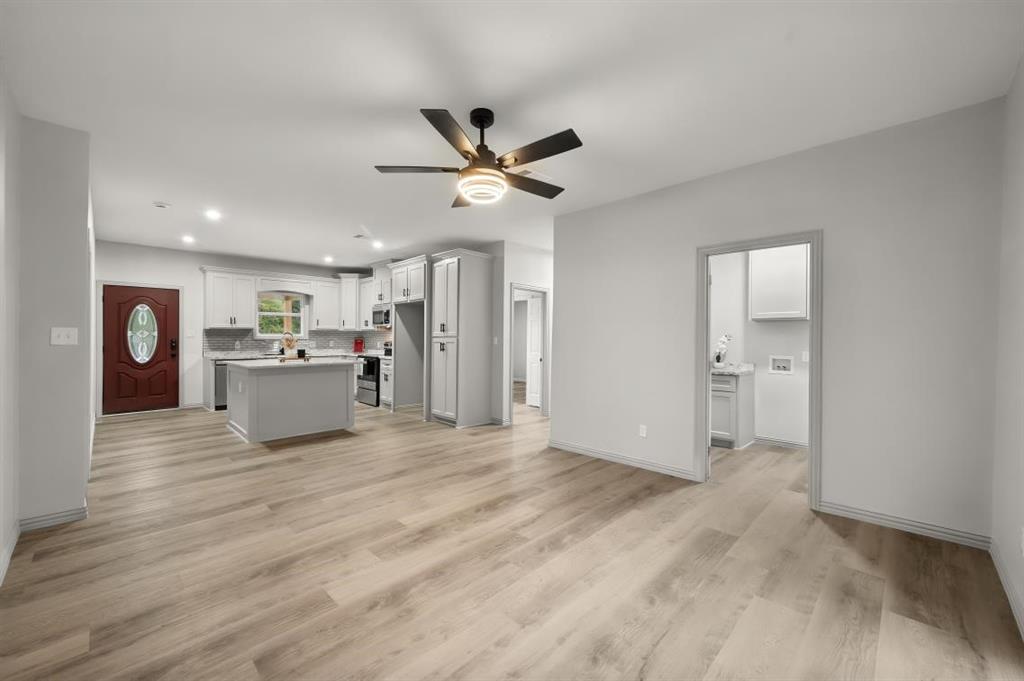 Open-concept interior featuring wood-finish flooring, a kitchen island, white cabinetry, and a ceiling fan with integrated lighting
