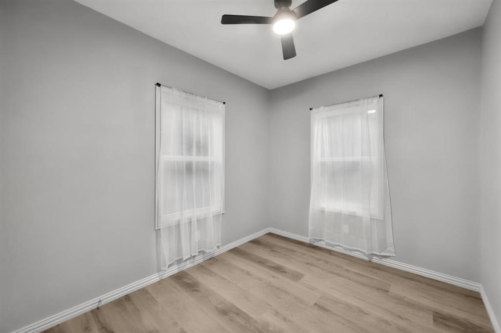 Unfurnished bedroom - Neutral interior space featuring wood-finish flooring, two double-hung windows, and a matte black ceiling fan with integrated lighting