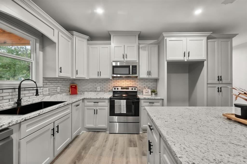 Kitchen featuring white shaker-style cabinetry, stone-finish countertops, subway tile backsplash, stainless steel appliances, and wood-finish flooring