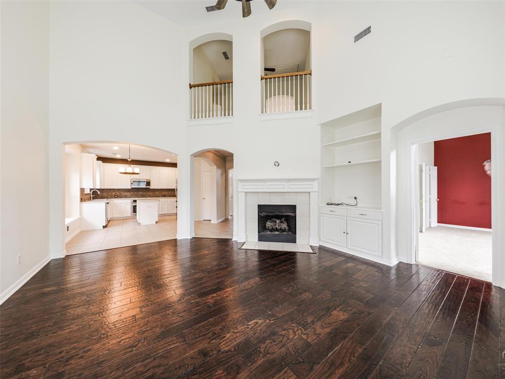 Expansive living area featuring vaulted ceilings, wood-finish flooring, a fireplace with a custom mantle, built-in shelving, and architectural arched openings