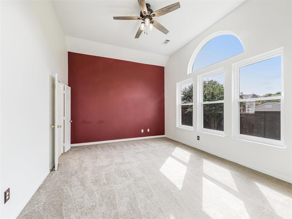 Primary bedroom features high ceilings, an arched window, a ceiling fan with integrated lighting, and carpeted flooring