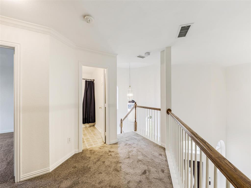 Landing area featuring carpeted flooring, white balustrade with wood-finish handrail, and pendant lighting