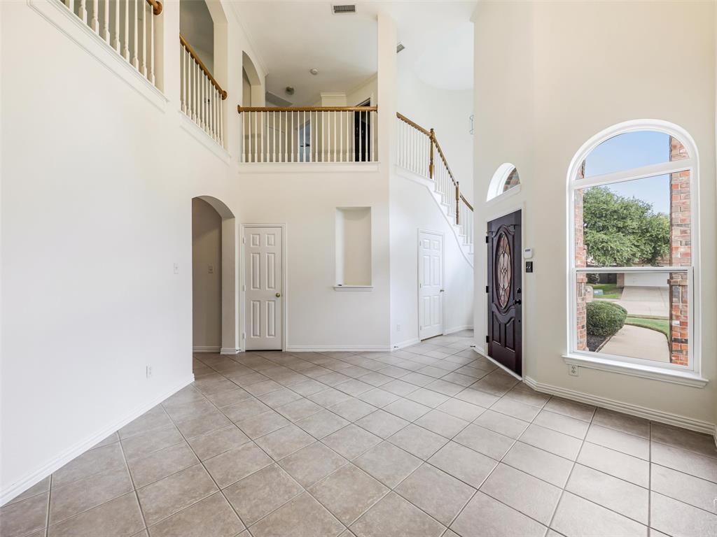 Front room with two-story foyer featuring tile flooring, an arched window, a built-in recessed niche, and a wooden staircase with a railed balcony