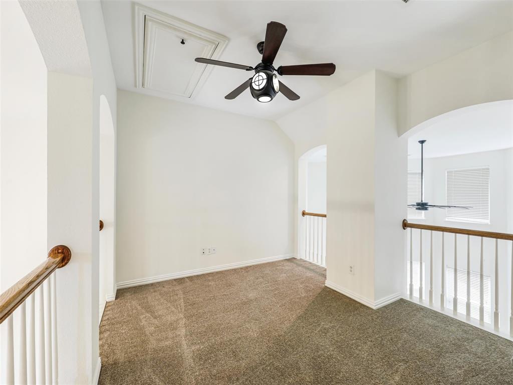 Neutral carpeted floor, ceiling fan with integrated lighting, arched architectural openings, and white balustrade railing