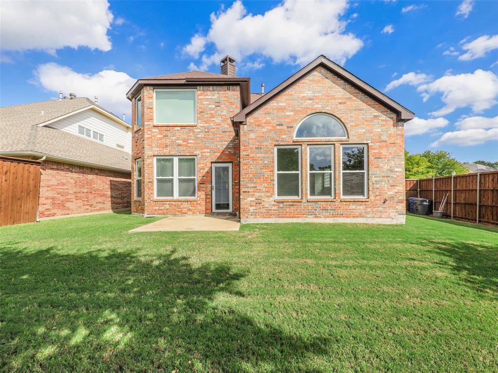 Multi-story brick exterior featuring a concrete patio, an arched transom window, a chimney, and a fenced backyard