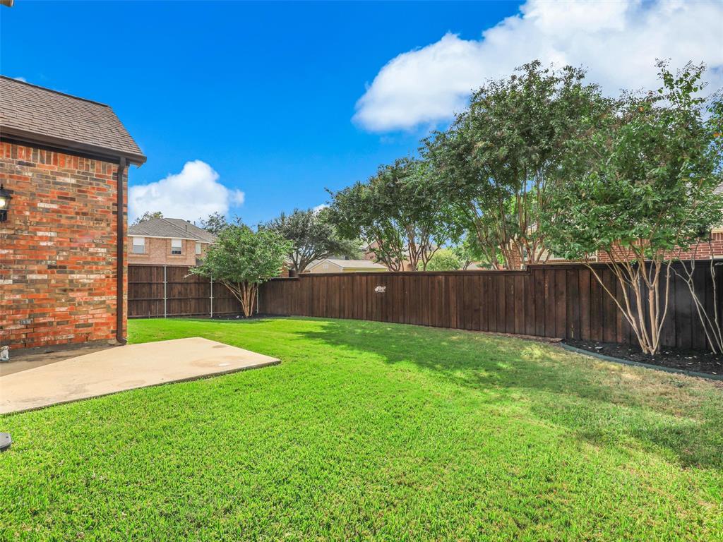 Backyard featuring a concrete patio, brick exterior wall, manicured lawn, and full-height wood privacy fencing