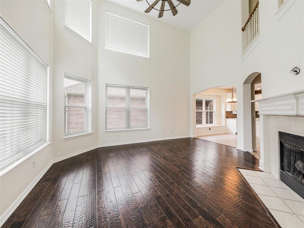 Two-story living area featuring vaulted ceilings, wood-finish flooring, a fireplace with a light-toned surround, an arched entryway, and a balcony overlook