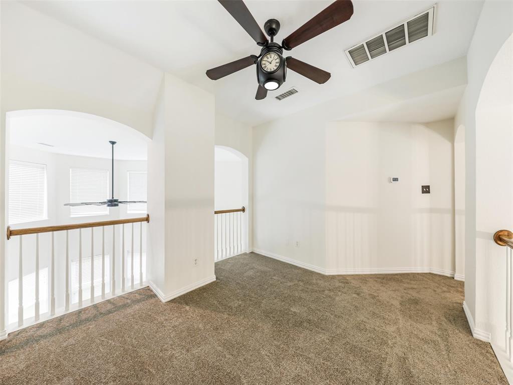 Neutral-toned carpeted flooring, vaulted ceiling with a central multi-blade ceiling fan, and decorative white archways featuring wood-capped white balustrade railings