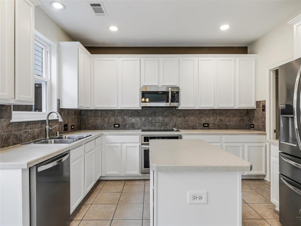 Kitchen featuring white shaker-style cabinetry, a central island with countertop seating, stainless steel appliances, tile backsplash, and ceramic tile flooring