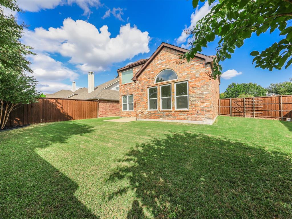 Brick exterior featuring a manicured lawn, wood privacy fencing, arched transom window, and stone-finish rear patio