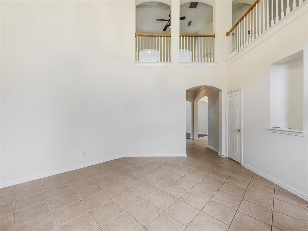 Two-story interior space featuring vaulted ceilings, tile flooring, an arched entryway, recessed wall niche, and an elevated landing with a white balustrade and wood-finish railing