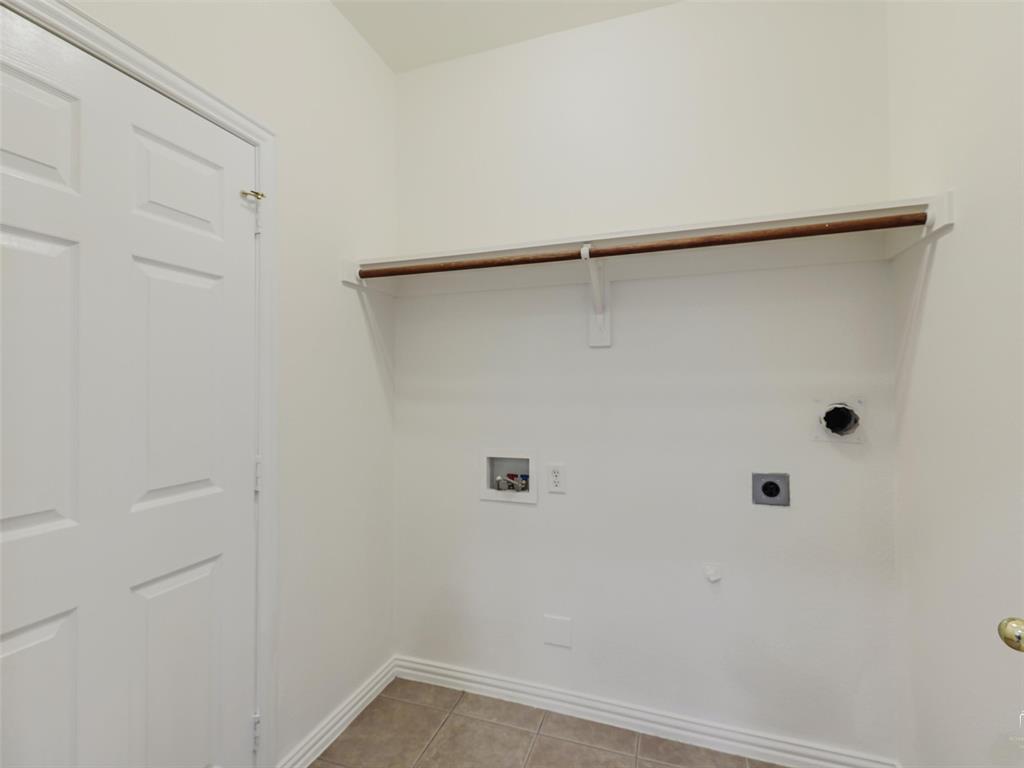 Dedicated laundry area featuring tile flooring, a built-in wall shelf with a hanging rod, and utility hookups