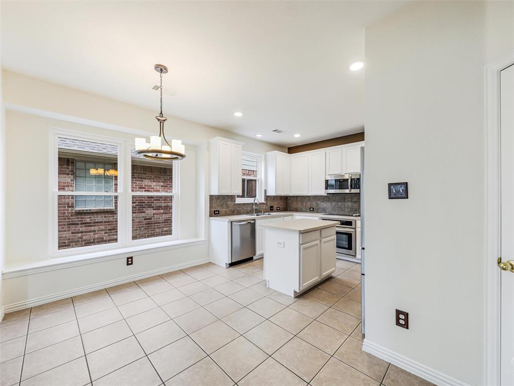 Kitchen featuring white shaker-style cabinetry, central island, tile flooring, stainless steel appliances, and a built-in window seat