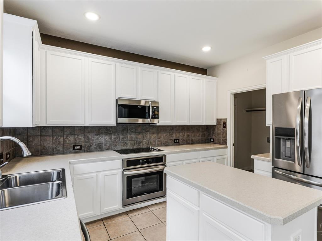 Kitchen featuring white shaker-style cabinetry, stone-finish countertops, stainless steel appliances, ceramic tile backsplash, and tile flooring