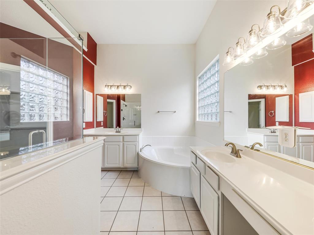Dual vanity with white cabinetry and solid-surface countertops, soaking tub, glass-enclosed shower, glass block windows, and ceramic tile flooring
