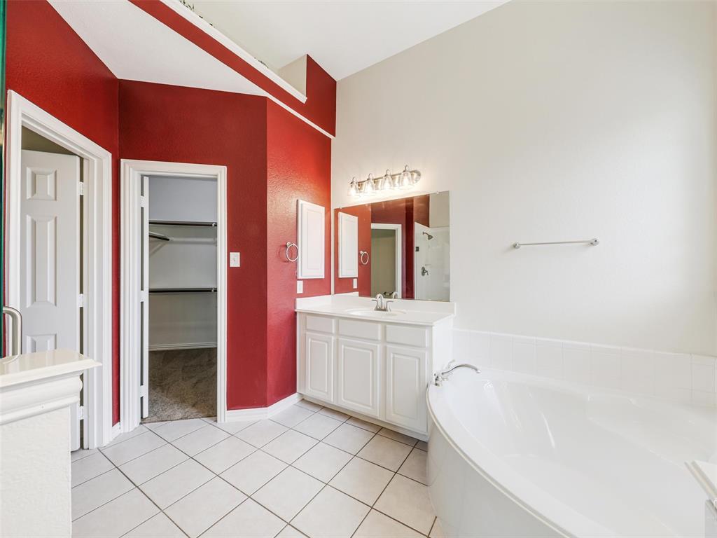 Bathroom featuring a white vanity cabinet with an integrated countertop and sink, wall-mounted mirror, multi-bulb lighting fixture, and a soaking tub