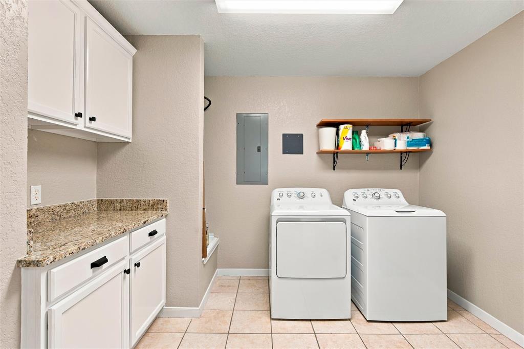 Laundry space featuring white cabinetry, stone-finish countertops, tile flooring, and wall-mounted shelving