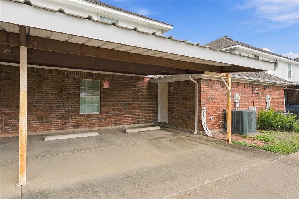 Covered carport featuring a concrete parking pad, brick exterior, and metal roof structure