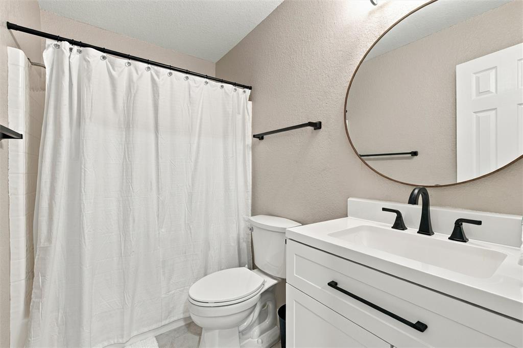 Bathroom featuring a white vanity with matte black hardware, integrated sink, oval wall-mounted mirror, and a combination tub and shower with matte black fixtures