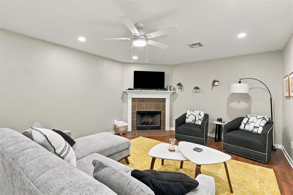 Fireplace with a tile surround and white mantel, wood-finish flooring, and recessed ceiling lighting