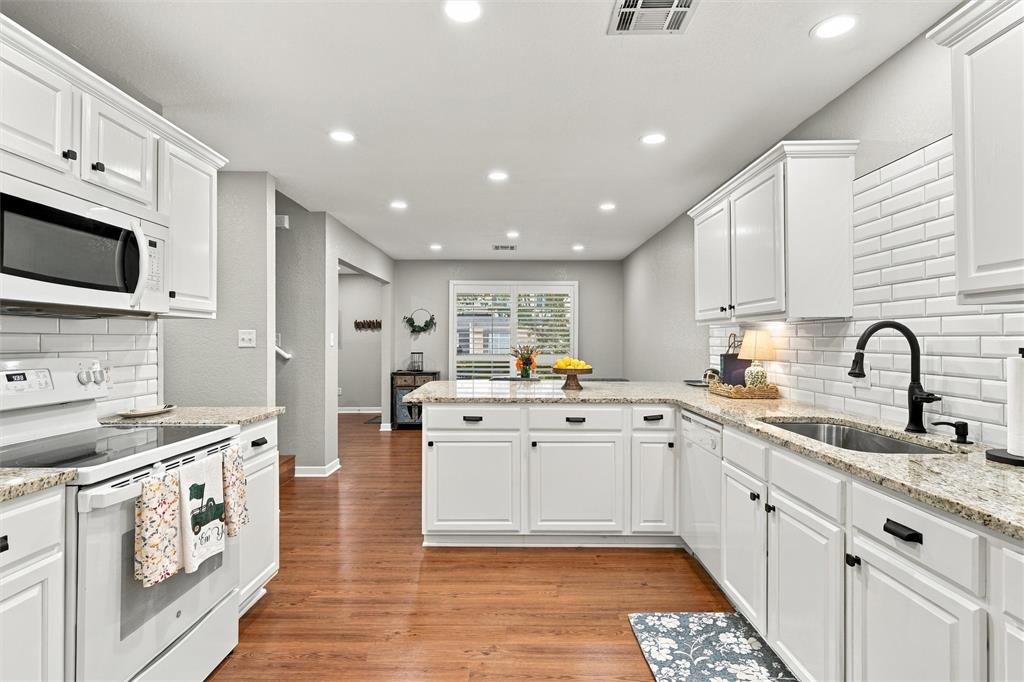 Kitchen featuring white cabinetry, stone countertops, white subway tile backsplash, matte black hardware, and wood-finish flooring