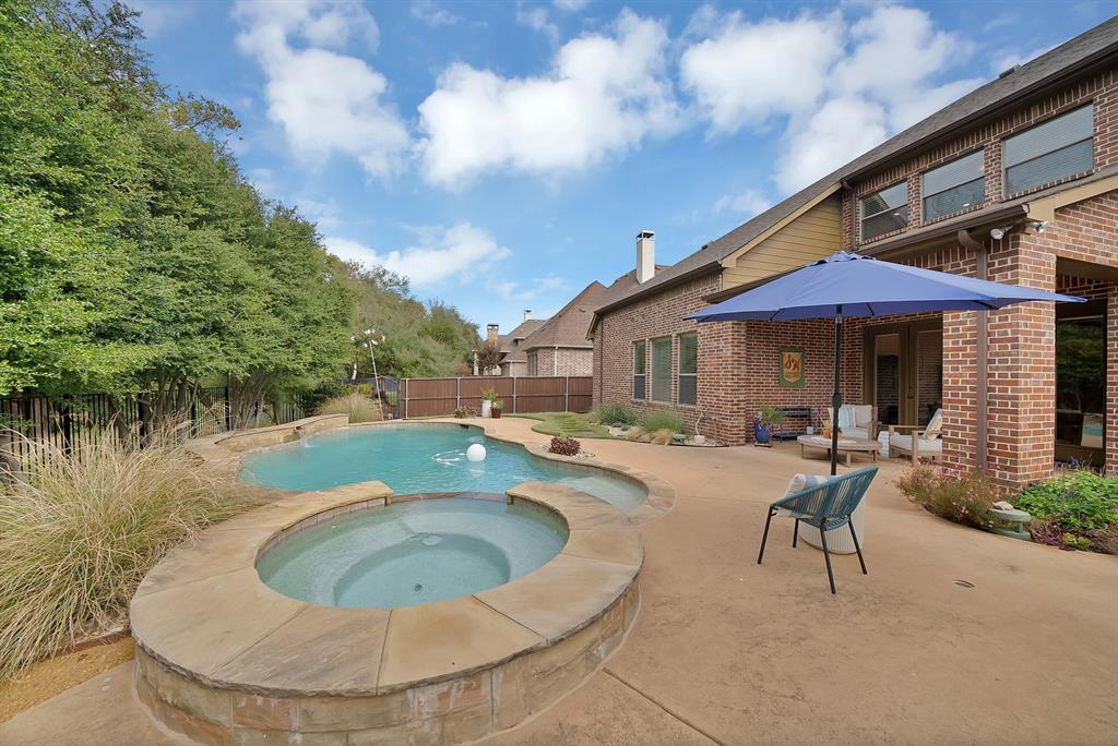 Brick exterior, inground swimming pool, elevated stone-capped spa, and expansive concrete patio