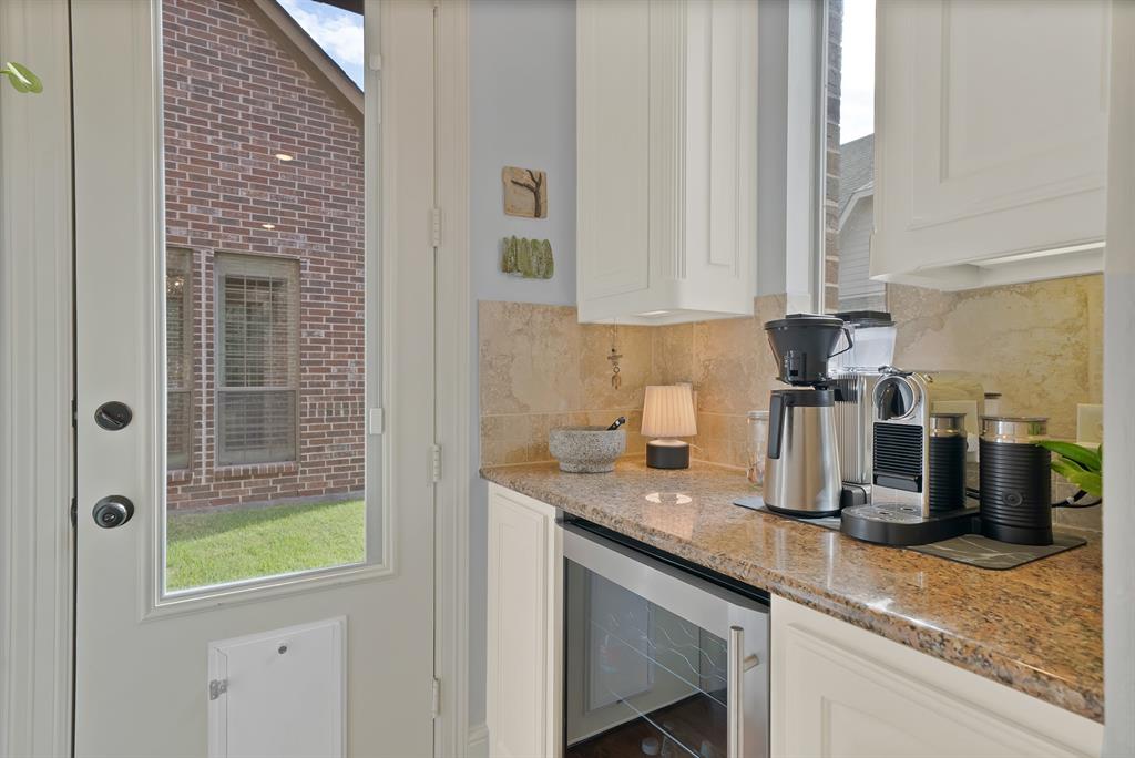 Custom cabinetry, stone-finish countertops, stone tile backsplash, and built-in under-counter beverage refrigerator