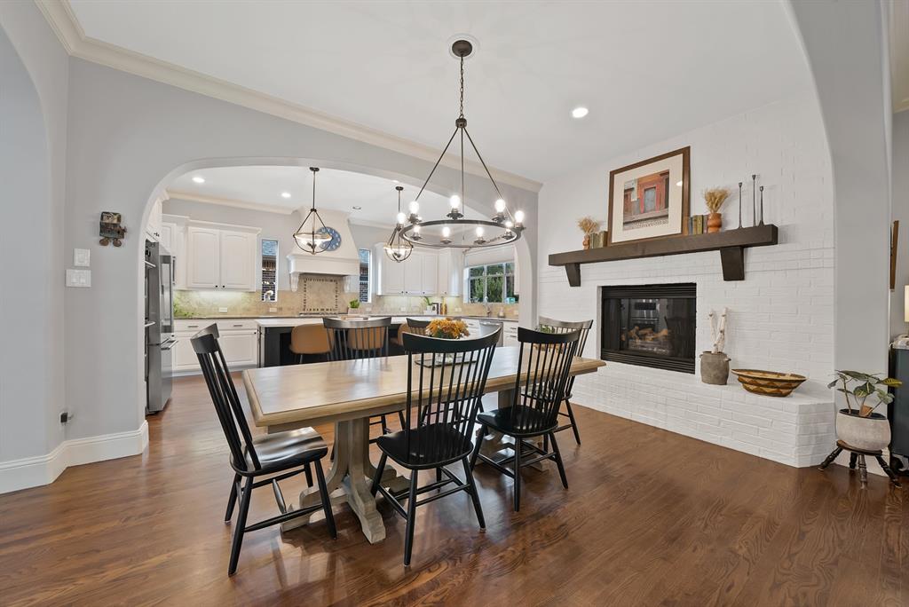 Dining space featuring wood-finish flooring, a white brick fireplace with a timber mantel, an arched wall opening, and a multi-light wrought iron chandelier