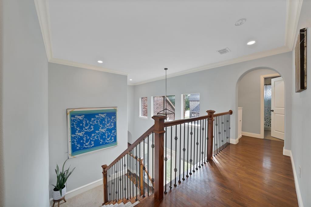 Upper landing featuring wood-finish flooring, a decorative metal baluster railing, recessed lighting, and a prominent arched entryway