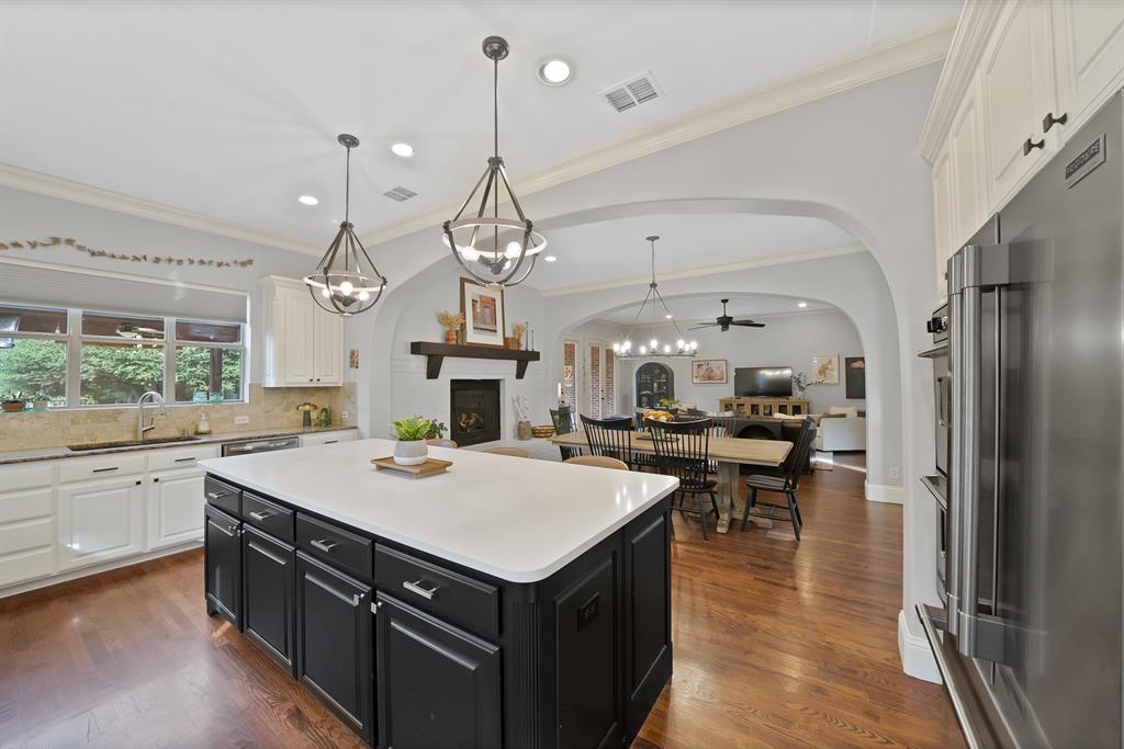 Kitchen featuring a central island with a solid surface countertop, wood-finish flooring, white and charcoal cabinetry, and dual geometric pendant lighting under arched architectural detailing