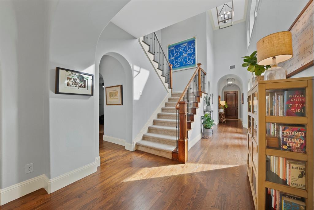 Foyer featuring arched architectural details, wood-finish flooring, a two-story ceiling, a staircase with decorative metal balusters, and a tiered hanging light fixture