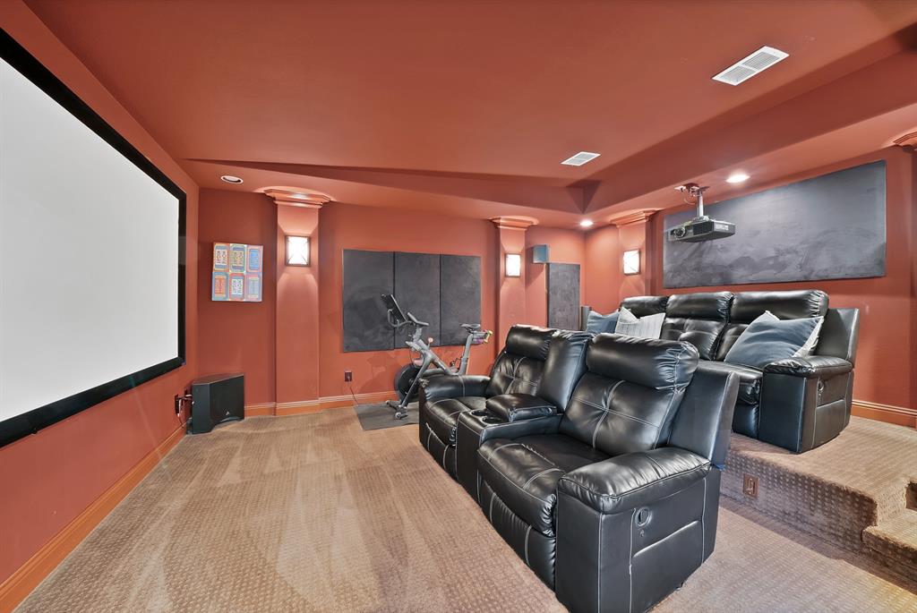 Media space featuring a large-format wall-mounted projection screen, tiered flooring, integrated wall sconce lighting, and decorative column accents