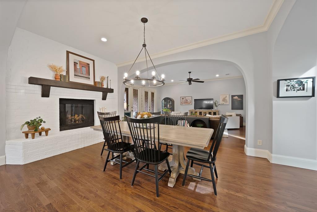 White brick fireplace featuring a dark wood mantel, wood-finish flooring, architectural arched opening, and an overhead multi-light chandelier