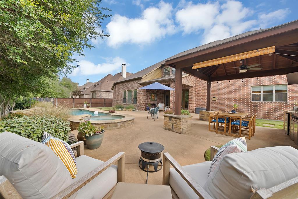 Brick exterior patio featuring a covered pavilion with a ceiling fan, a built-in outdoor kitchen, and an in-ground swimming pool with an integrated spa