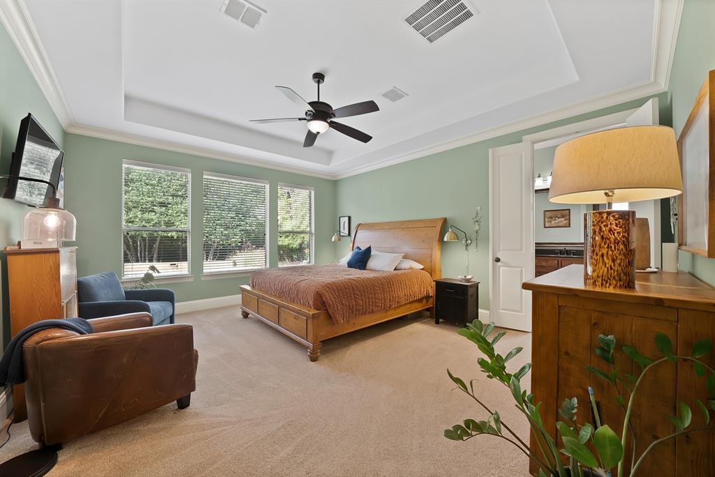 Tray ceiling with crown molding, ceiling fan, triple windows, and neutral carpeting