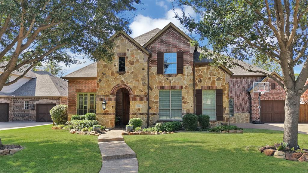 Multi-story exterior featuring a brick and stone facade, arched entryway, multi-gabled roofline, decorative window shutters, and a concrete walkway
