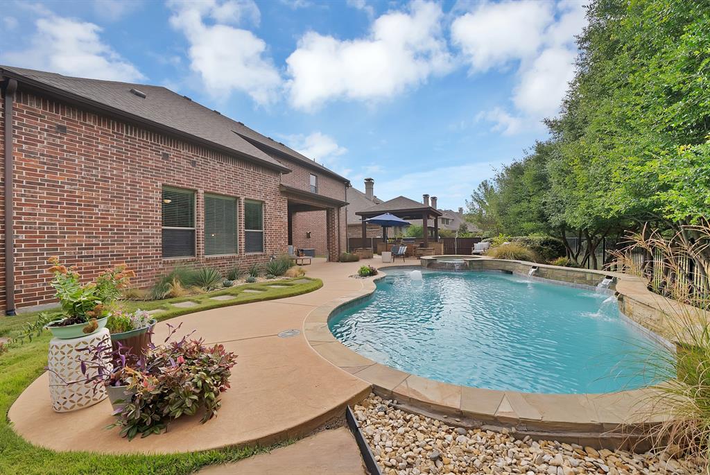 Brick exterior, expansive concrete patio, in-ground swimming pool with stone-accented water features, attached hot tub, and detached covered patio structure