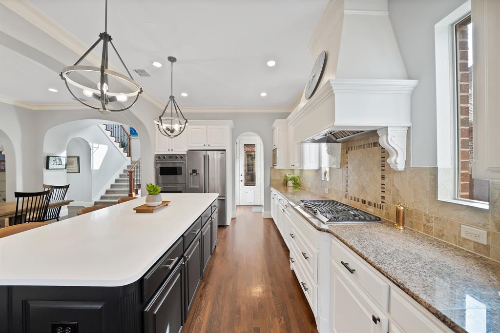 Kitchen featuring a large central island with solid-surface countertop, custom cabinetry, stainless steel double wall ovens, gas cooktop, and stone tile backsplash