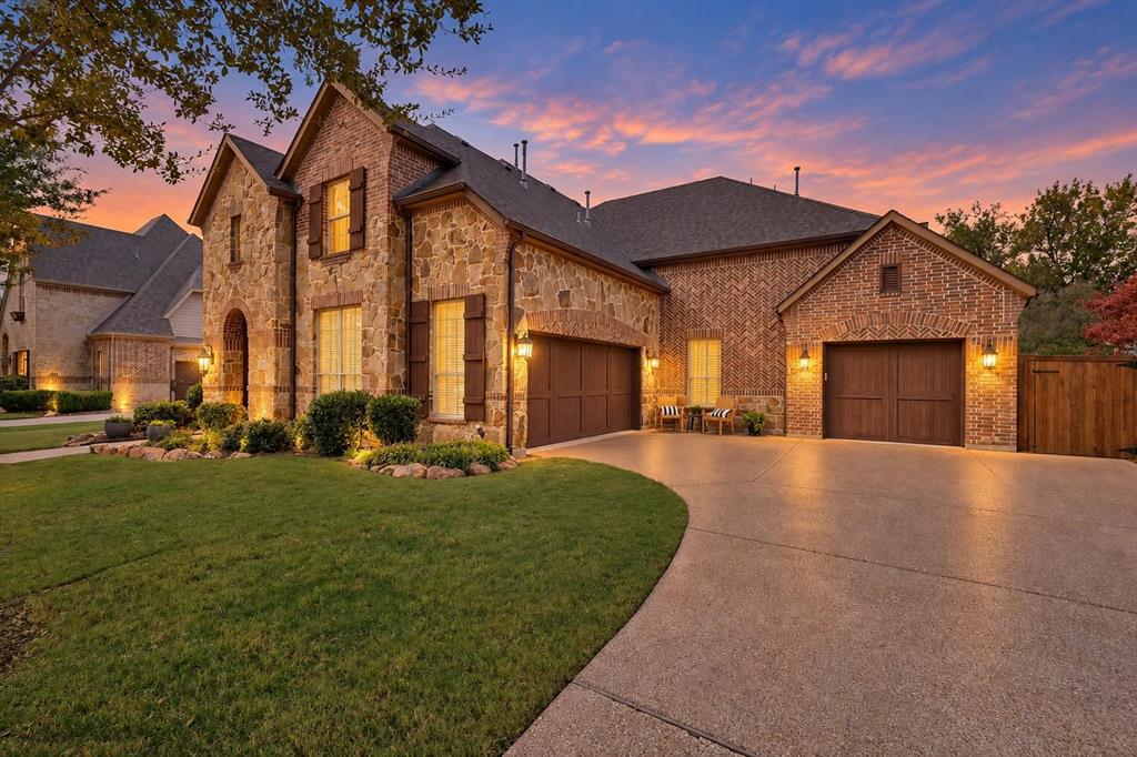 Stone and brick exterior facade featuring a multi-car garage, steep roof lines, wood-finish shutters, and professional landscape edging